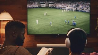 Sonos Ace headphones worn by a man watching TV, while another man reads next to him