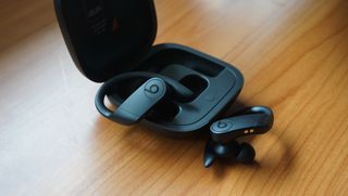 The Beats Powerbeats pro buds pictured next to their charging case on a wooden surface.