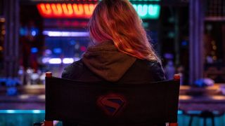 An image of Milly Alcock sitting on a chair with her back to camera on the set of Supergirl: Woman of Tomorrow