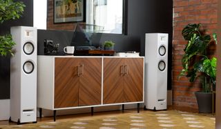 Pair of white floorstanding speakers on either side of wooden cabinet and turntable.