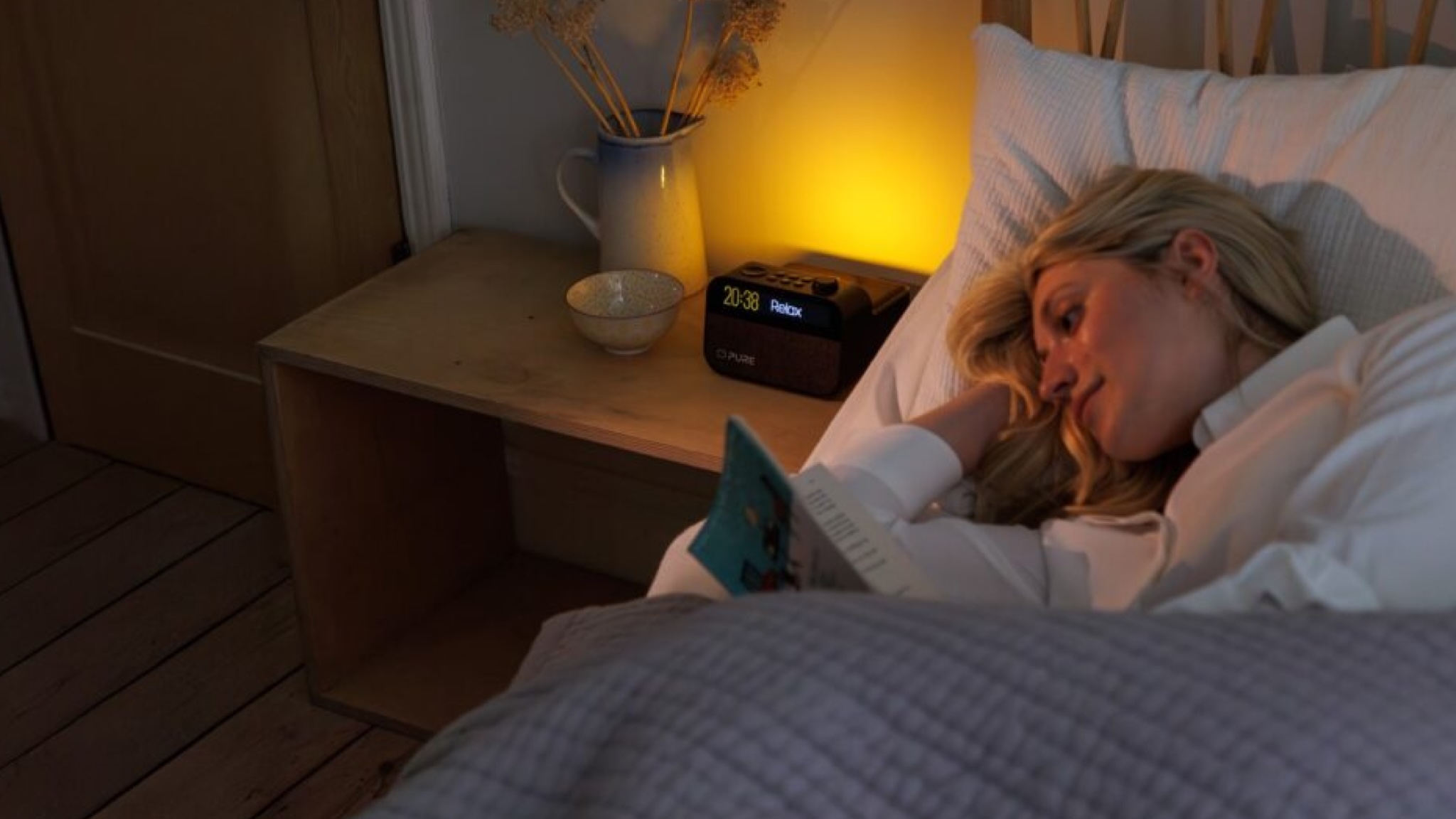 A woman reads in bed with light from her Pure Moment sleep companion