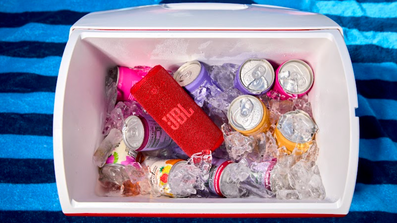 JBL Grip in a cooler filled with drinks cans, on a blue striped beach towel