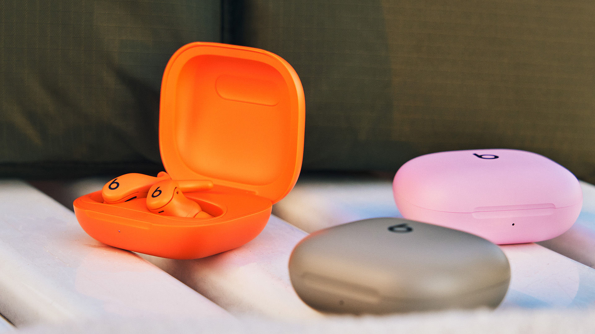 The Powerbeats Fit in orange, gray and pink, on a bench outdoors