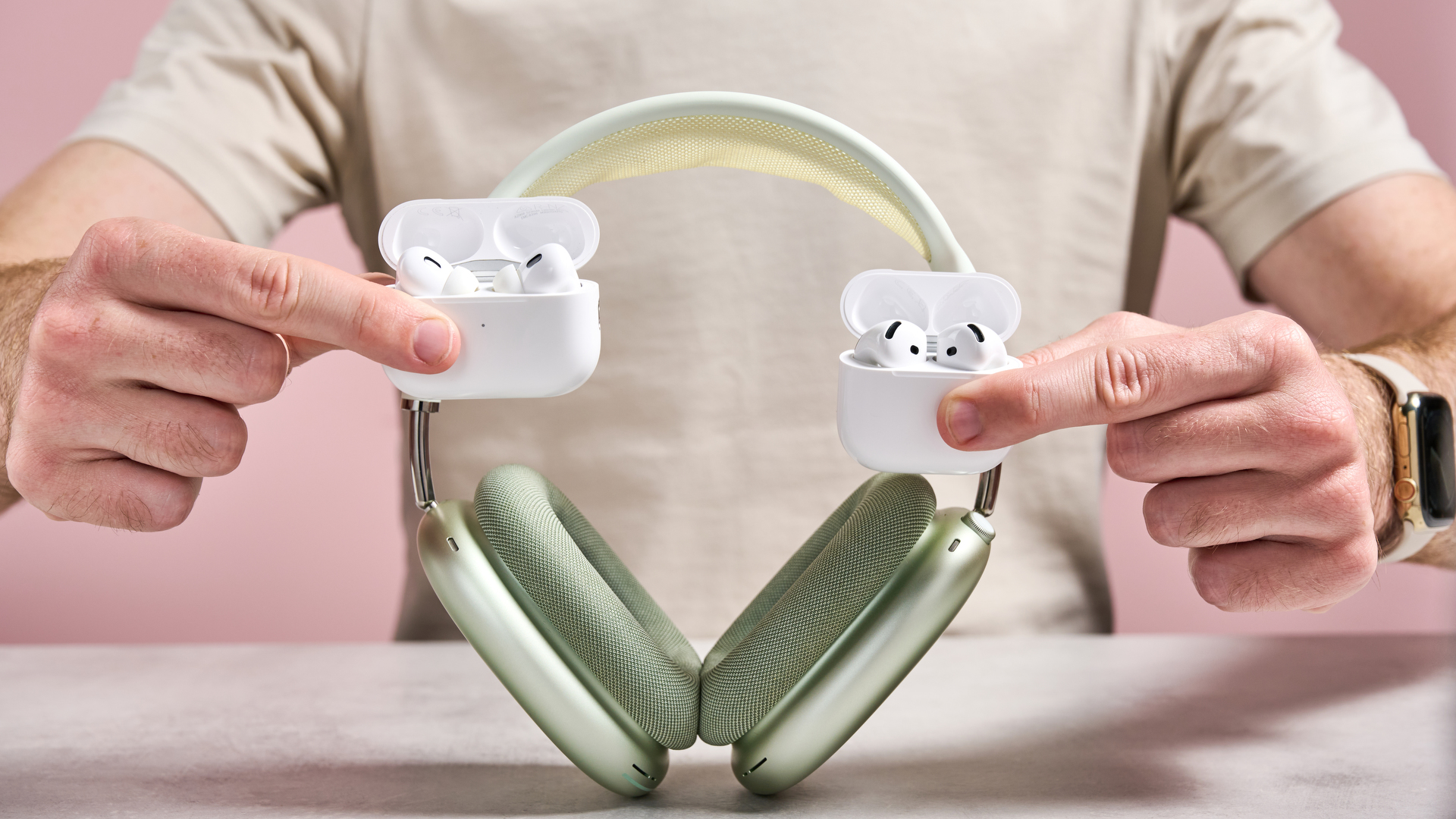 AirPods Pro 2, AirPods 4 and AirPods Max being held together in front of a man&#039;s torso