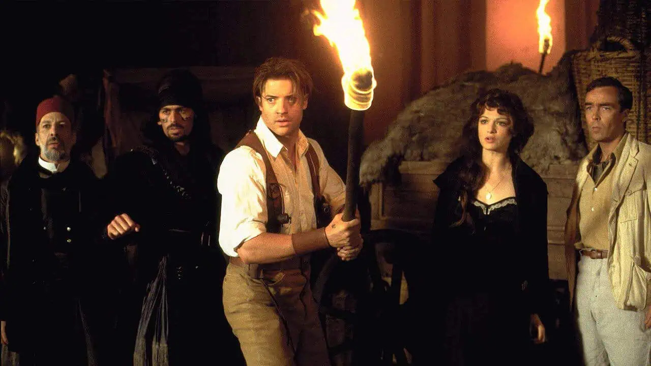 A group of treasure hunters holding fire torches in a tomb in The Mummy
