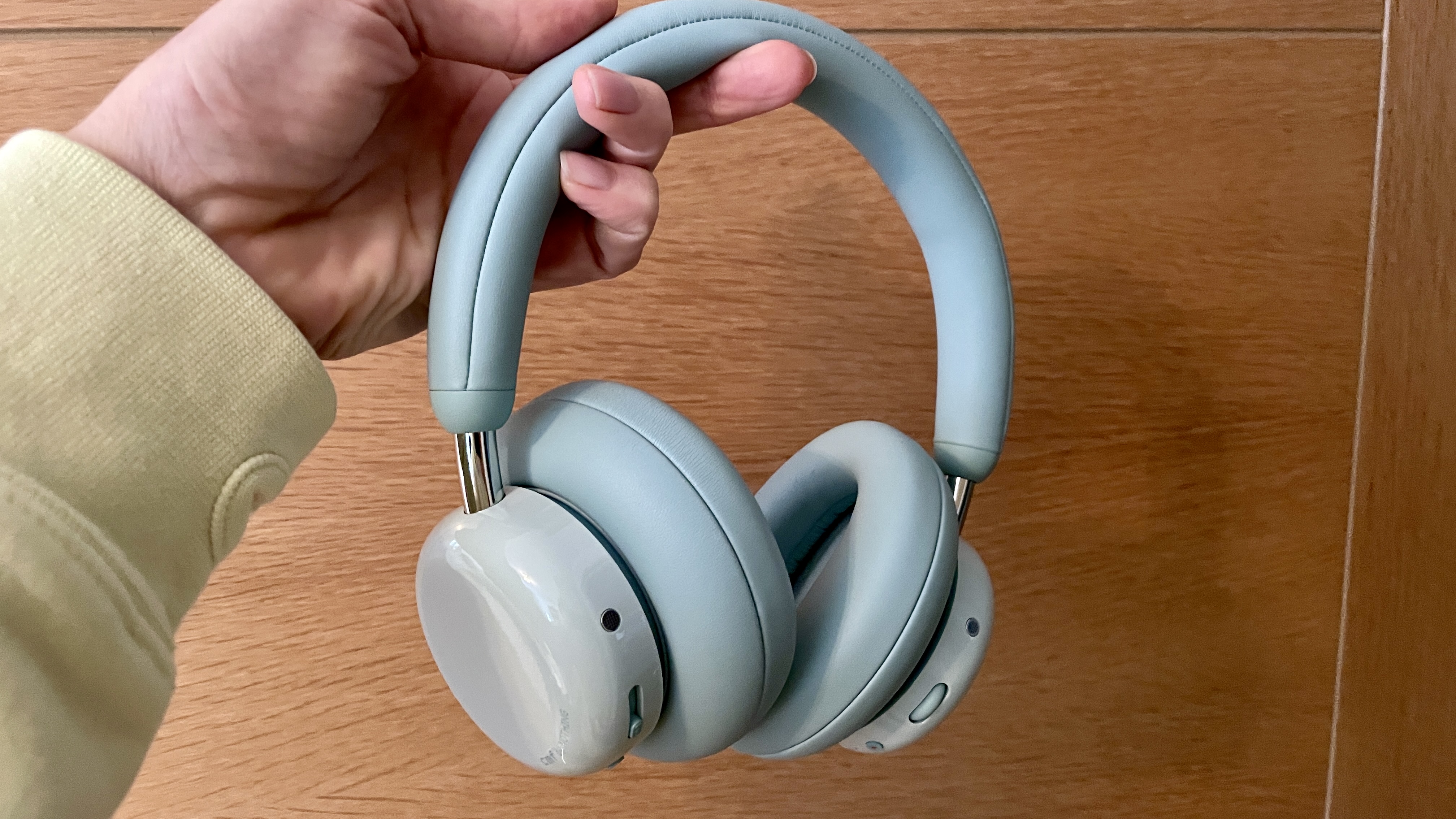 CMF Headphone Pro in pistachio green held in a hand or hung on a barbell, being pushed up by a carved frog