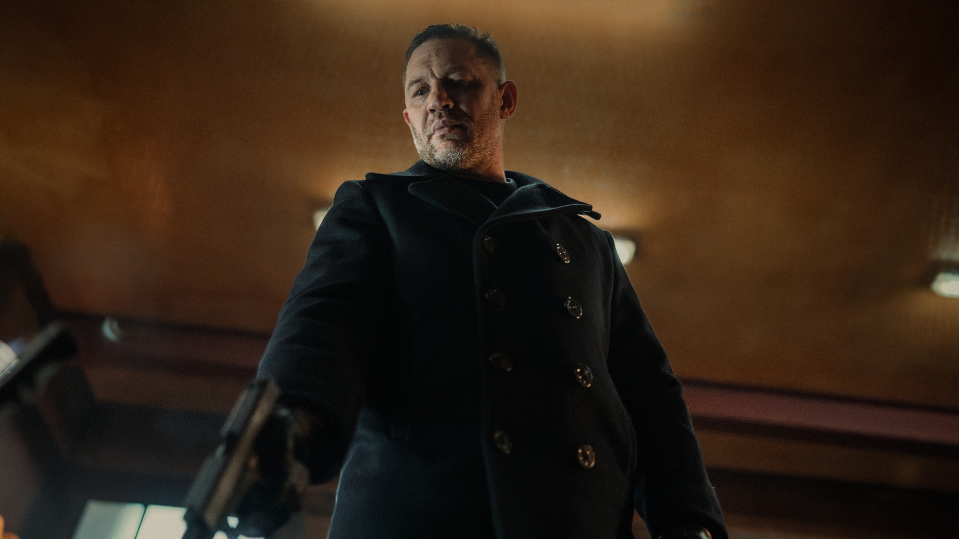 Harry points a gun to the floor in MobLand