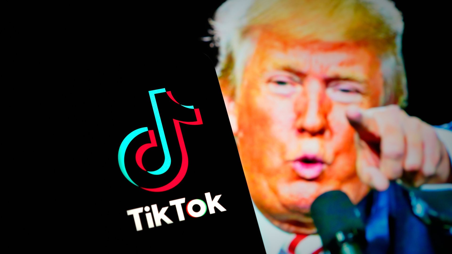 The TikTok logo is seen on a mobile device, with a picture of US President Trump in the background