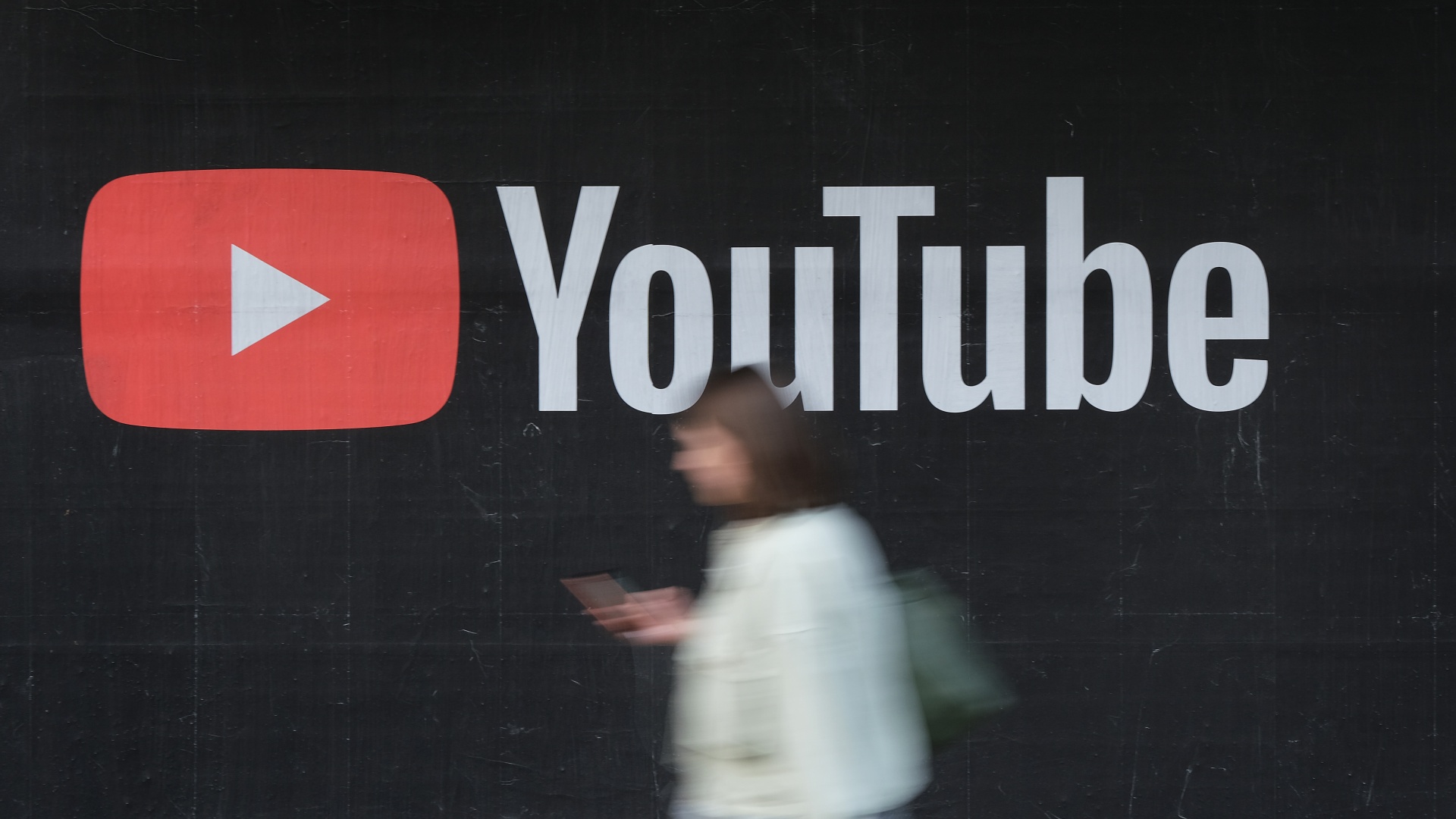 A woman with a smartphone walks past a billboard advertisement for YouTube on September 27, 2019 in Berlin, Germany