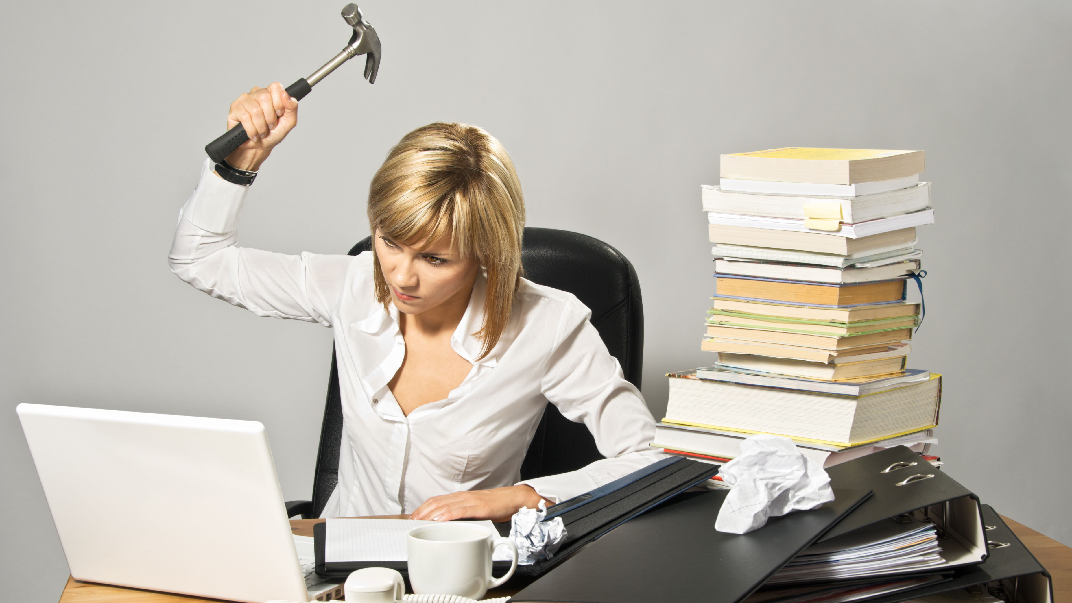 Angry business lady hitting a laptop with a hammer.