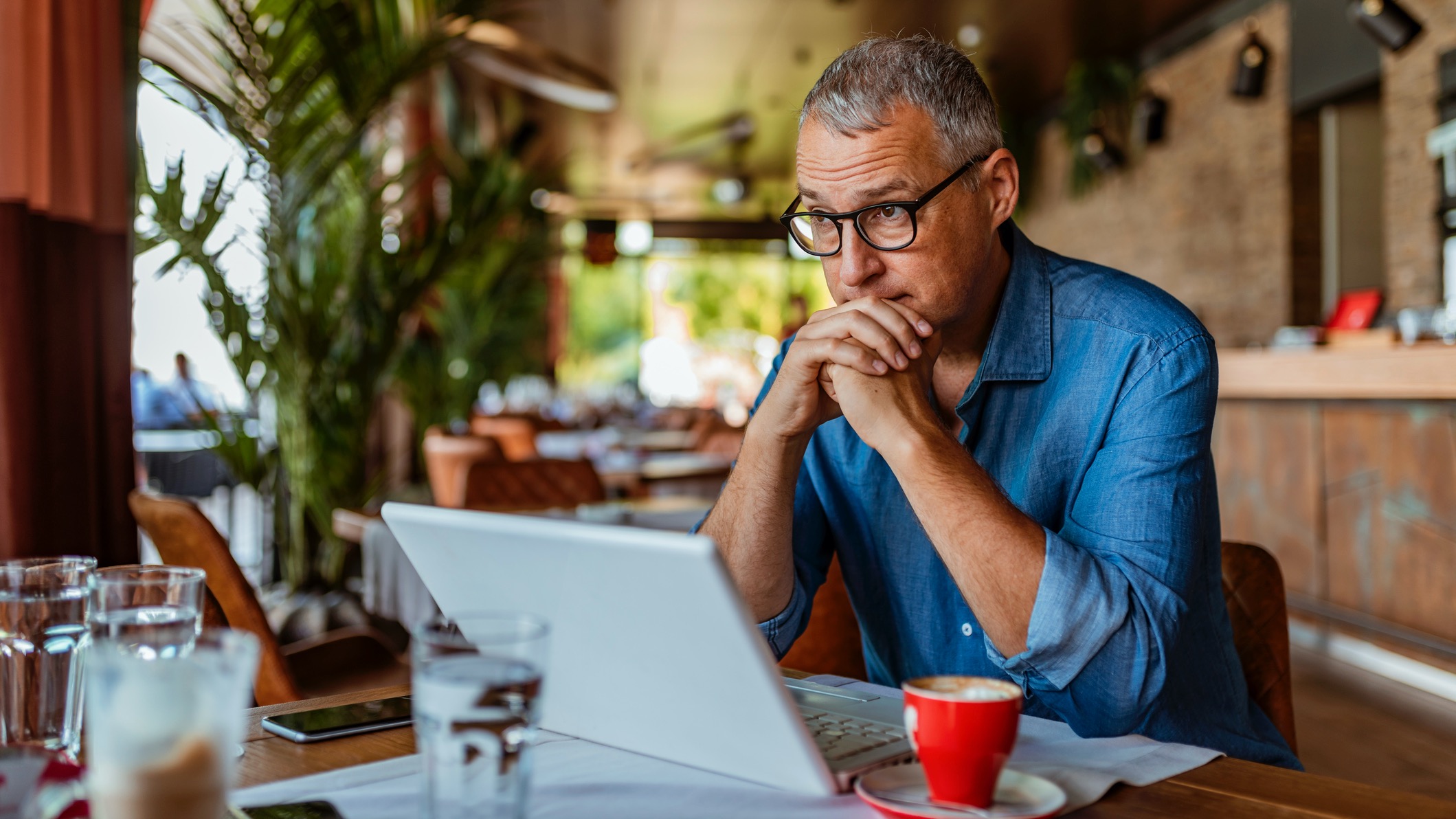 Mature man using Windows 11 laptop in a cafe, looking mildly annoyed