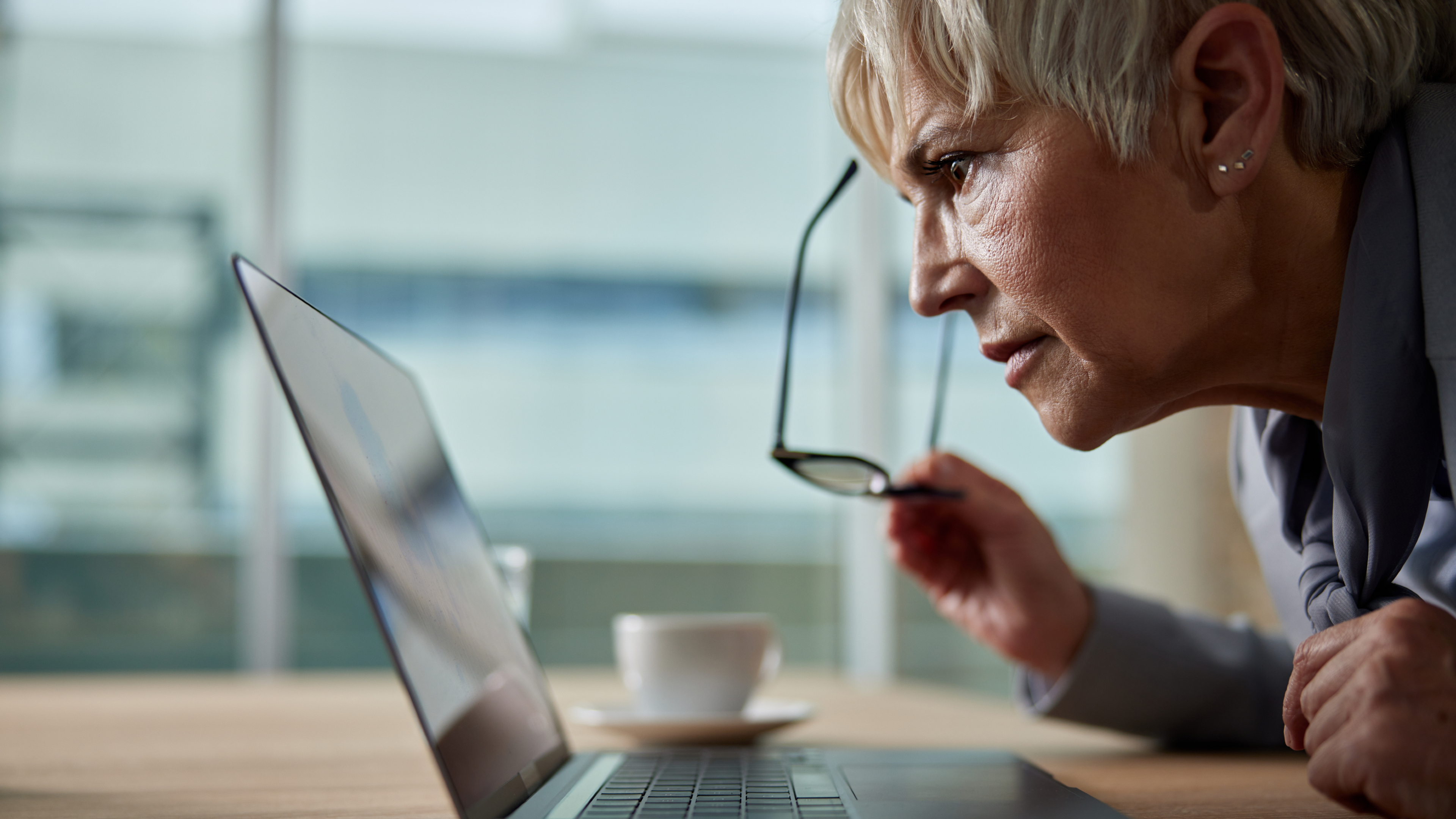 Woman looks at laptop on desk with glasses taken off
