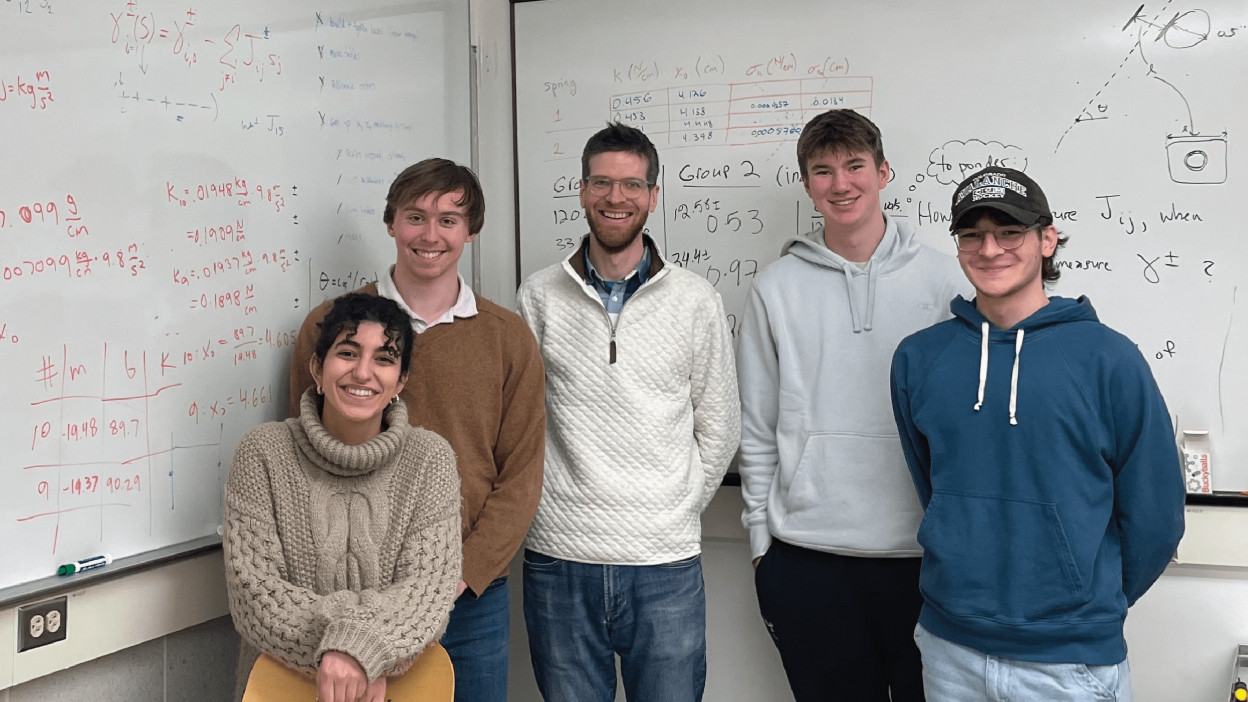 Scientists that made the mechanical computing platform shown standing in front of a marker board