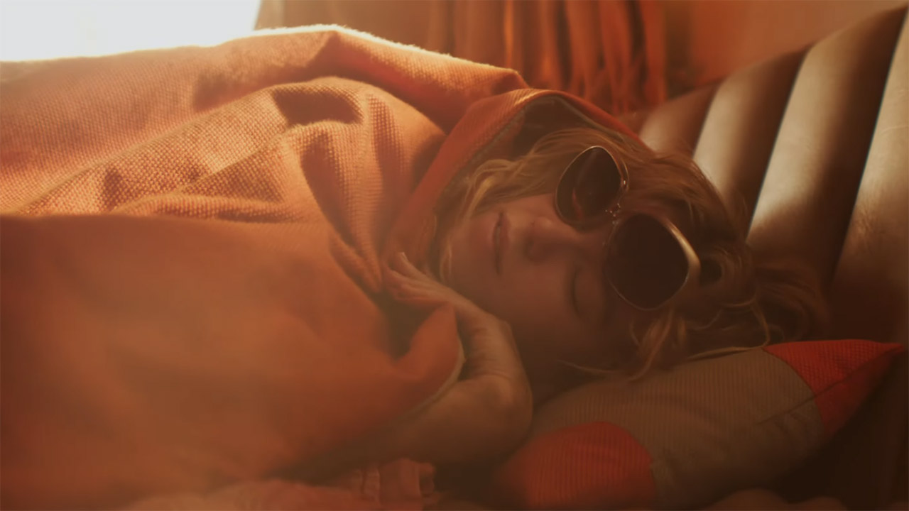 A hungover Kara Zor-El wearing sunglasses and lying in bed in Supergirl
