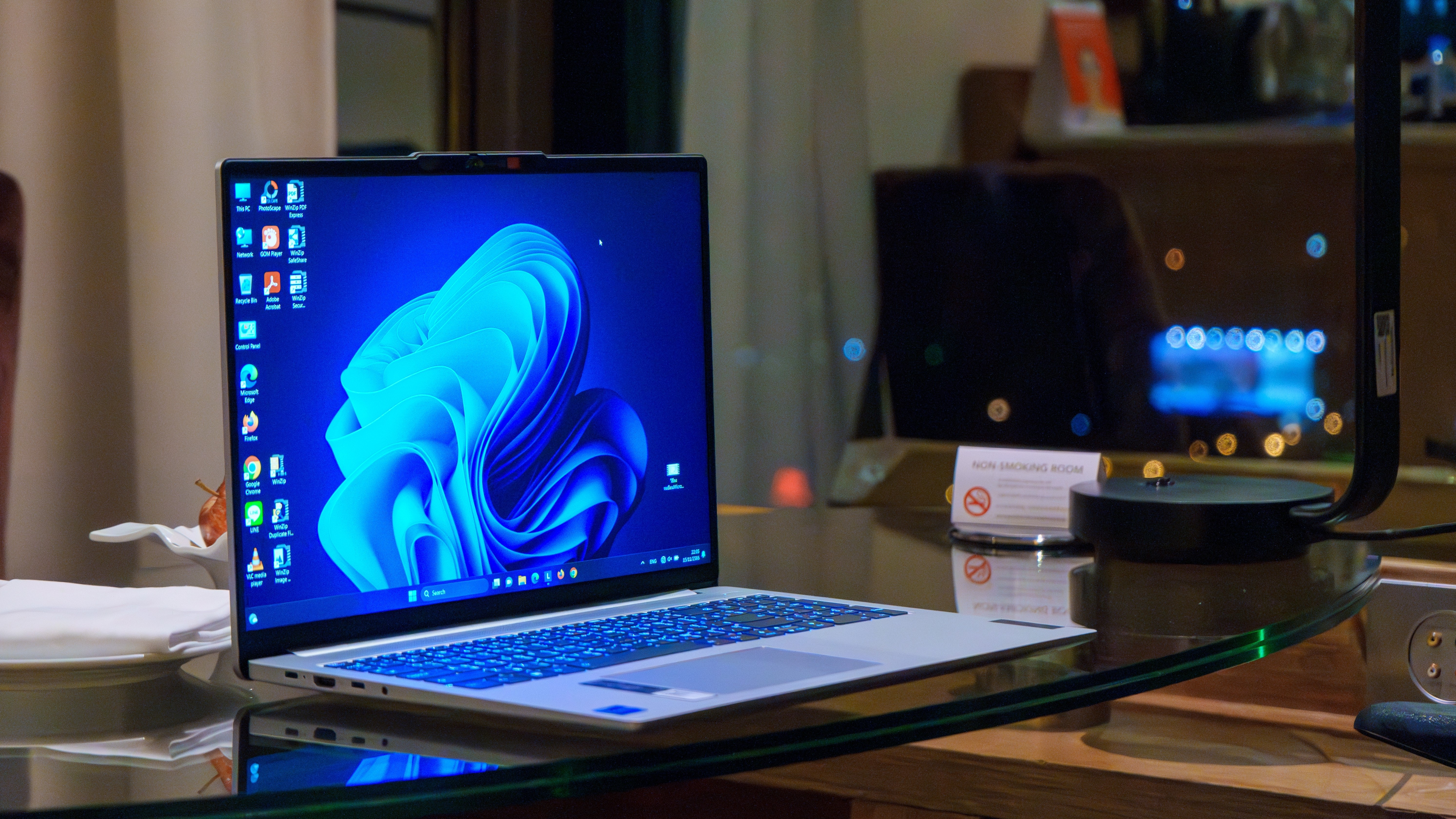 A laptop with the Windows 11 desktop on screen, glowing, while on a work desk