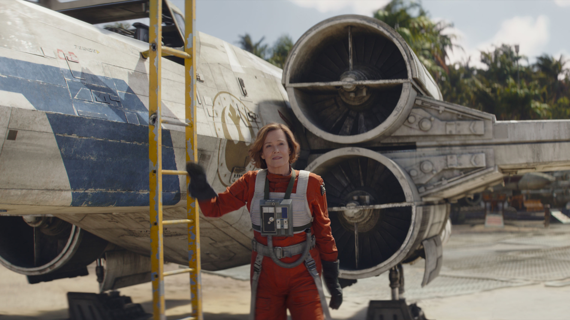 Sigourney Weaver's Colonel Ward holding onto a ladder next to an X-Wing in The Mandalorian and Grogu