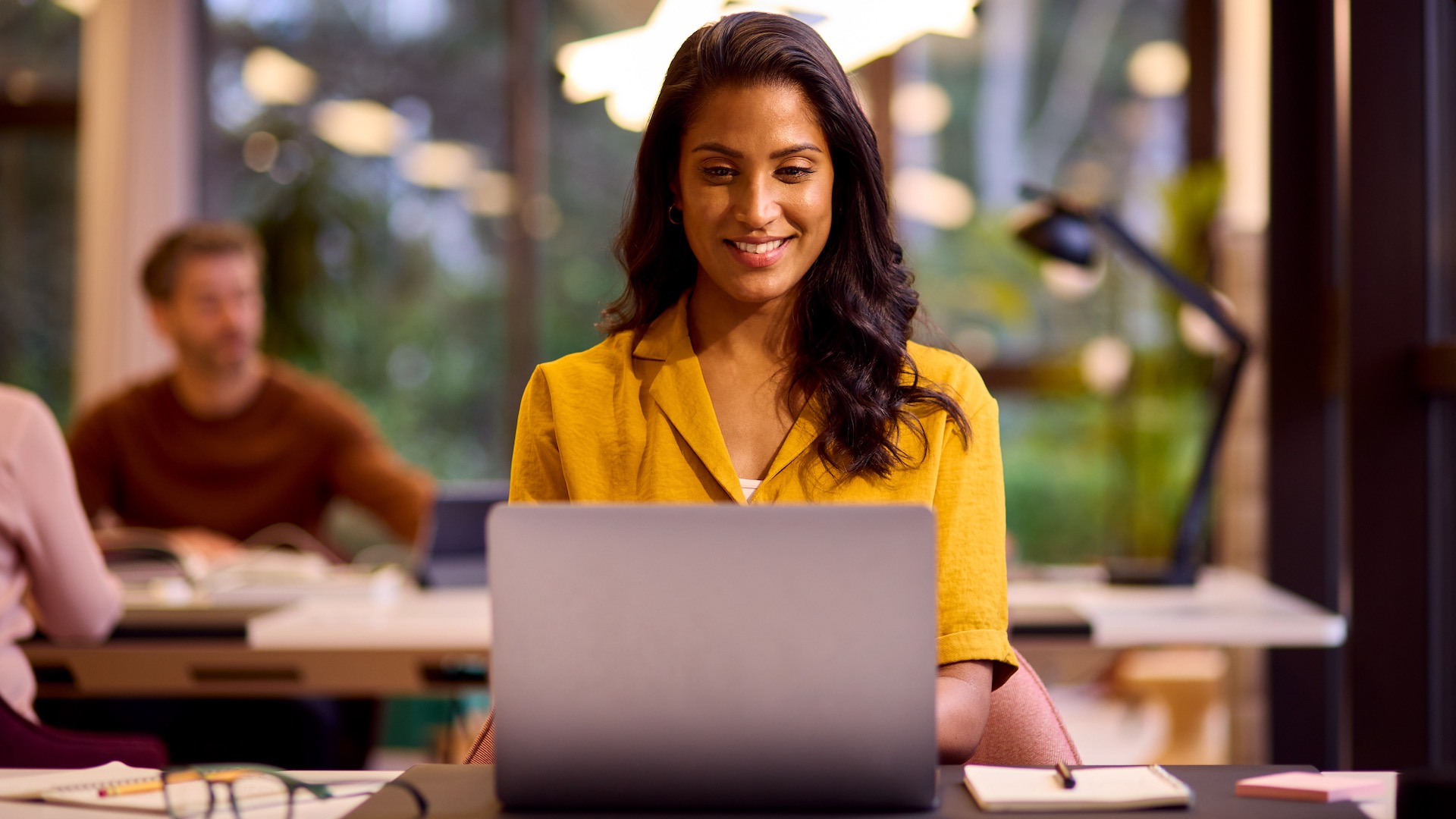 A young woman is working on a Windows 11 laptop in a relaxed office space.