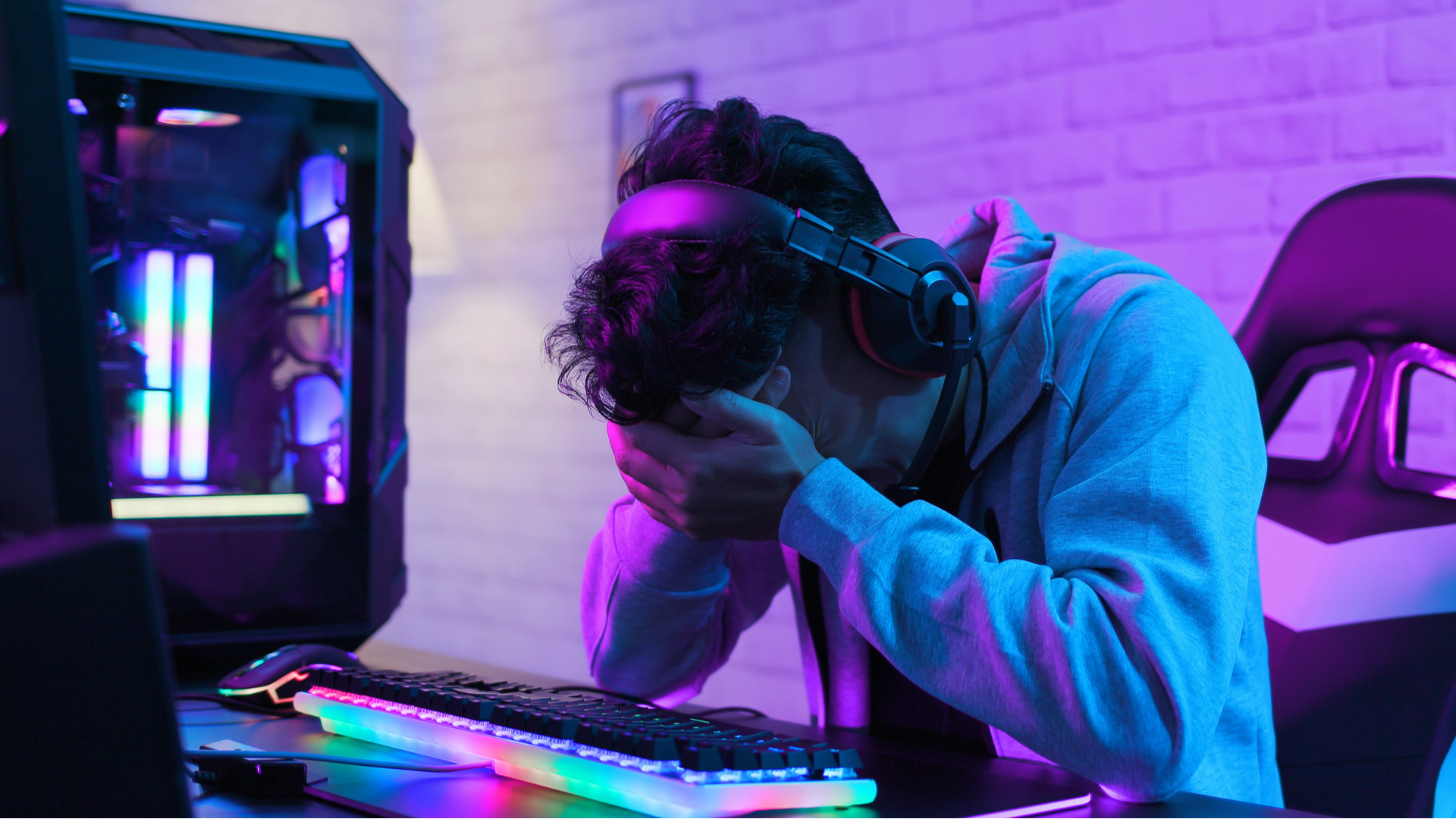 Sad looking person holding head in hands sat at a gaming PC