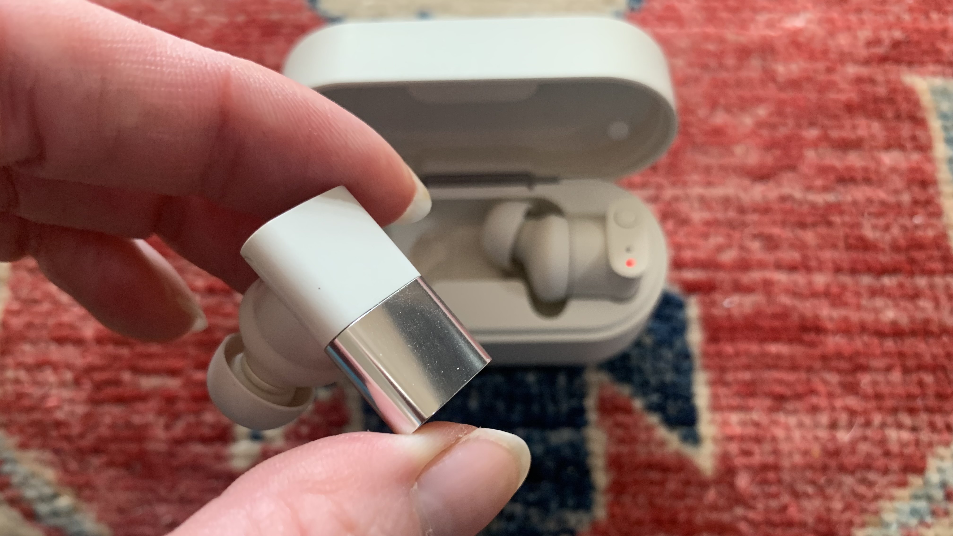 Status Between 3ANC earbud held on a colorful background