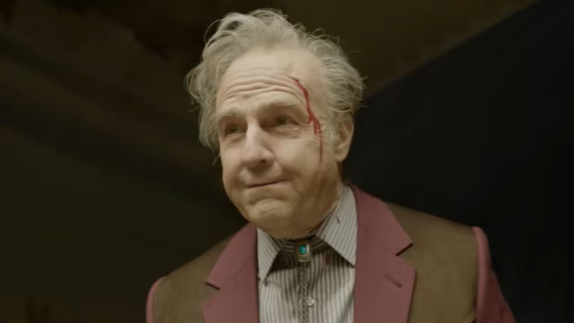 An aged version of Tom Cruise stands with a gash on his forehead